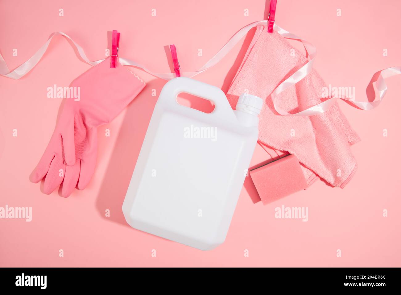 Creative idea for advertising cleansing product. A white plastic canister of detergent with rubber glove and scouring pads hung on a ribbon using clot Stock Photo