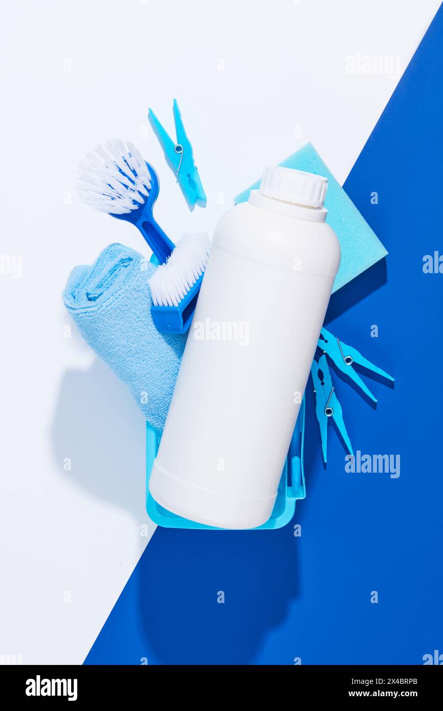 Top view of plastic basket full with wiper, brushes, sponge and clothespins. In the middle is an unbranded white bottle mockup for detergent product a Stock Photo