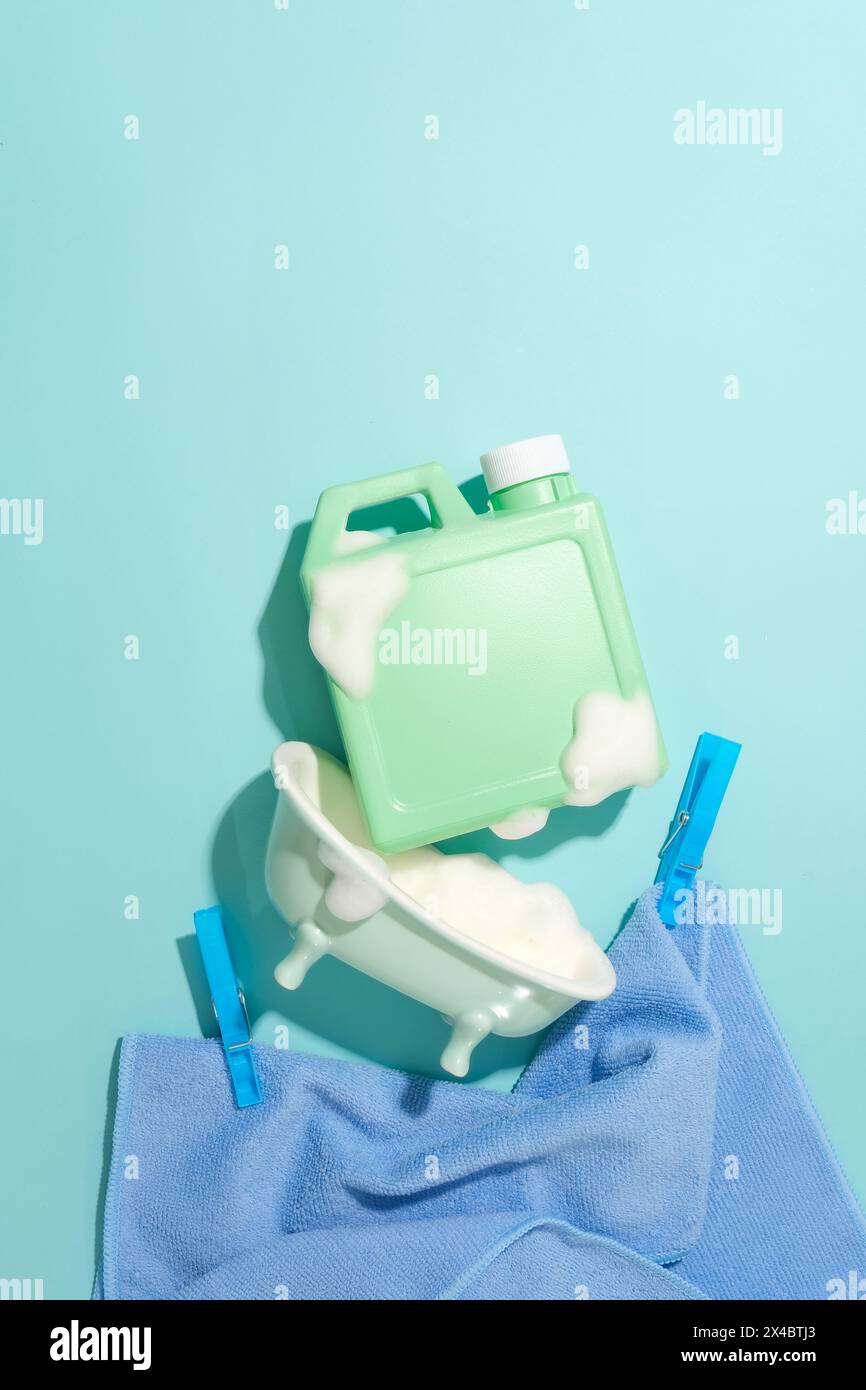 A bottle of detergent with white foam, a mini bathtub, two clothespins and a cotton towel on a blue background. Mockup for cleaning product advertisem Stock Photo