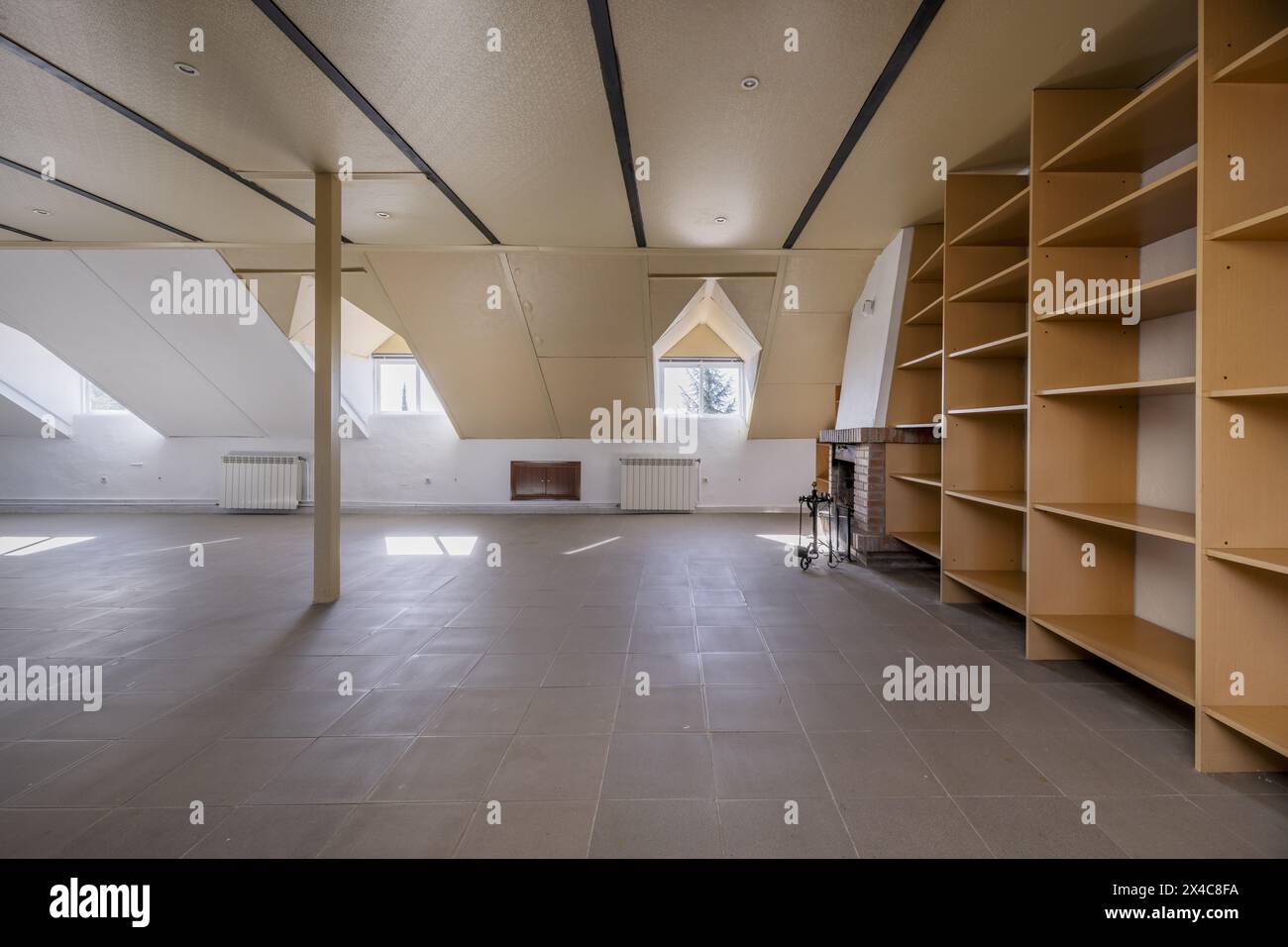 Large attic of a house with a wall covered with wooden shelves with skylights with windows Stock Photo