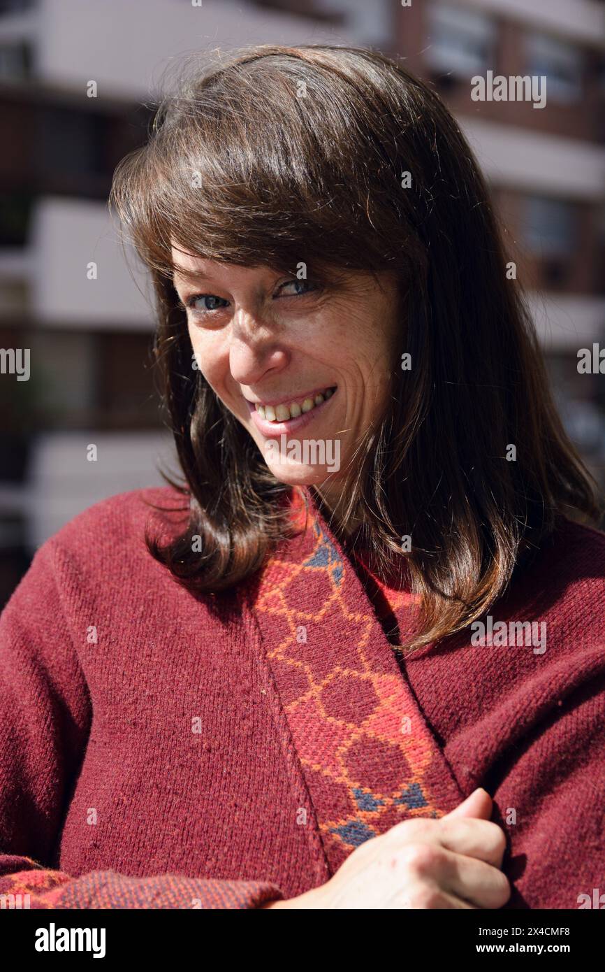 vertical image of portrait of Latin adult woman looking at camera smiling very funny covering herself with her sweater sunbathing in morning and looki Stock Photo