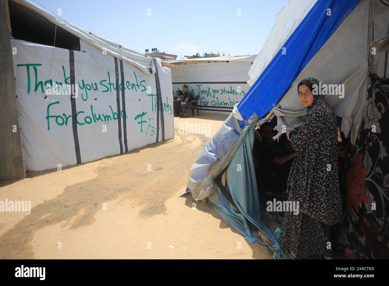 Displaced Palestinian woman stand next a tent, adorned with slogans ...