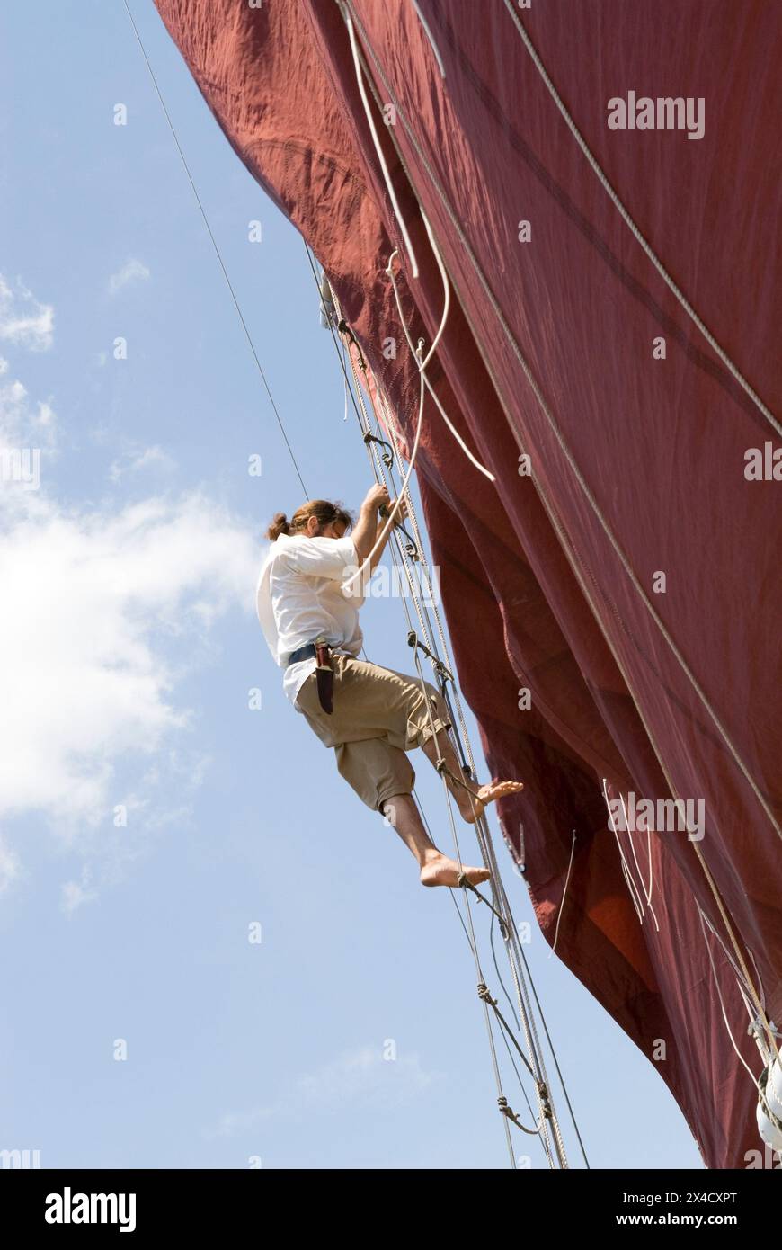 A pirate in full costume climbs a rope ladder on the Jolly Rover tall ship, which is docked on the riverfront in Georgetown, South Carolina, USA. Stock Photo