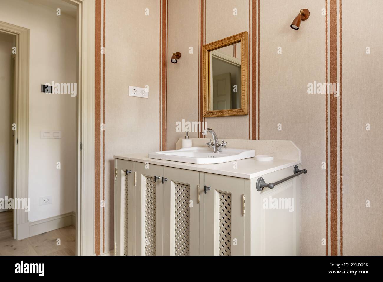 Modern design bathroom with cream marble sink, rectangular mirror with golden wooden frame, and matching walls with decorative wallpaper Stock Photo