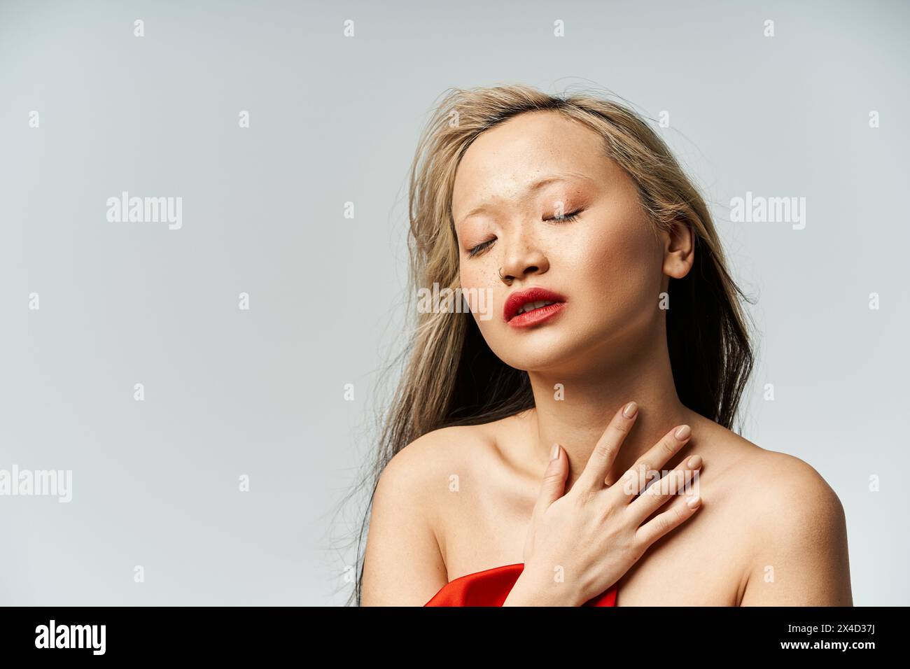 An attractive Asian woman in a vibrant red dress, eyes closed in a serene pose. Stock Photo