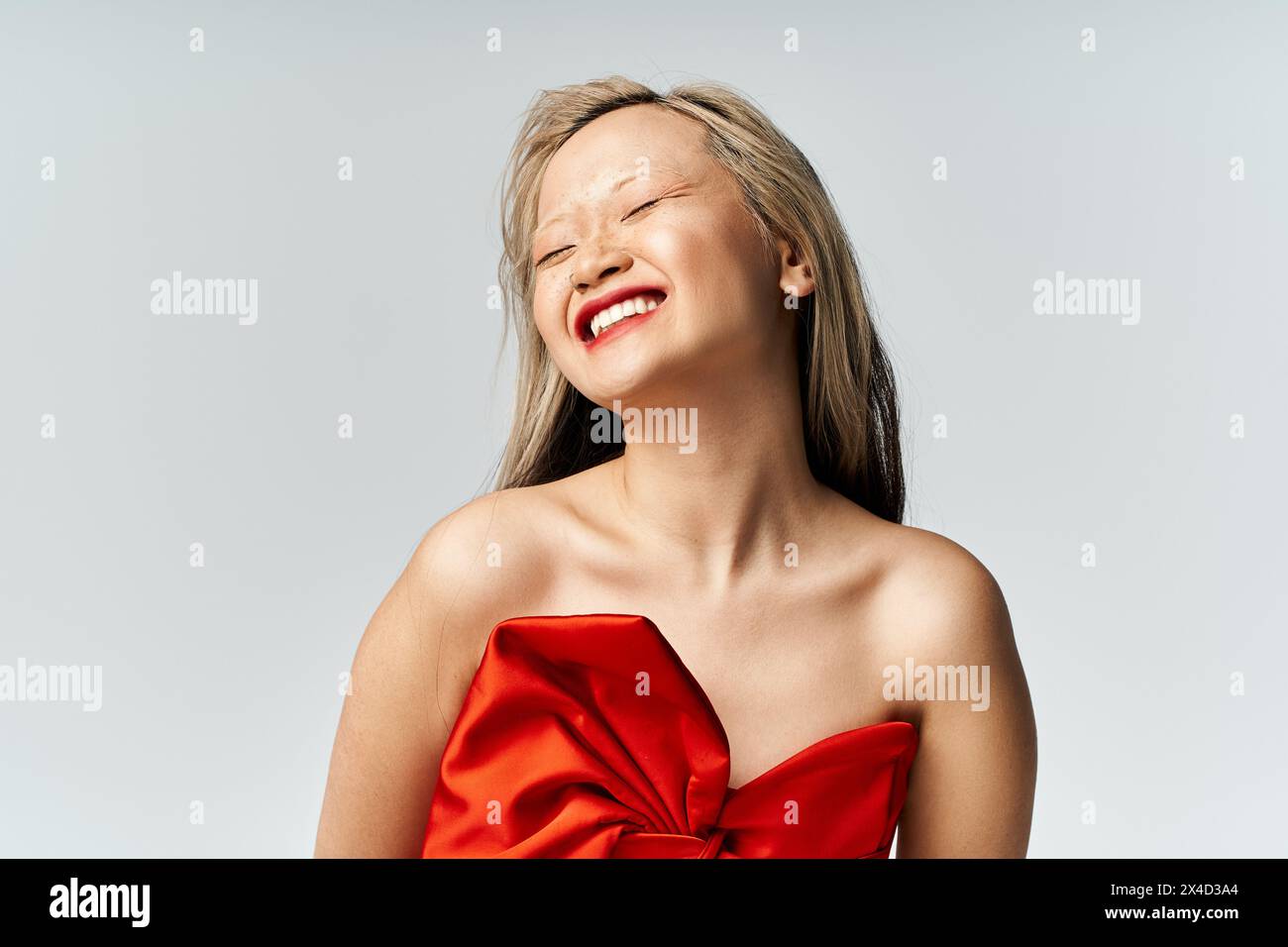 Asian woman in red dress laughs, eyes closed. Stock Photo