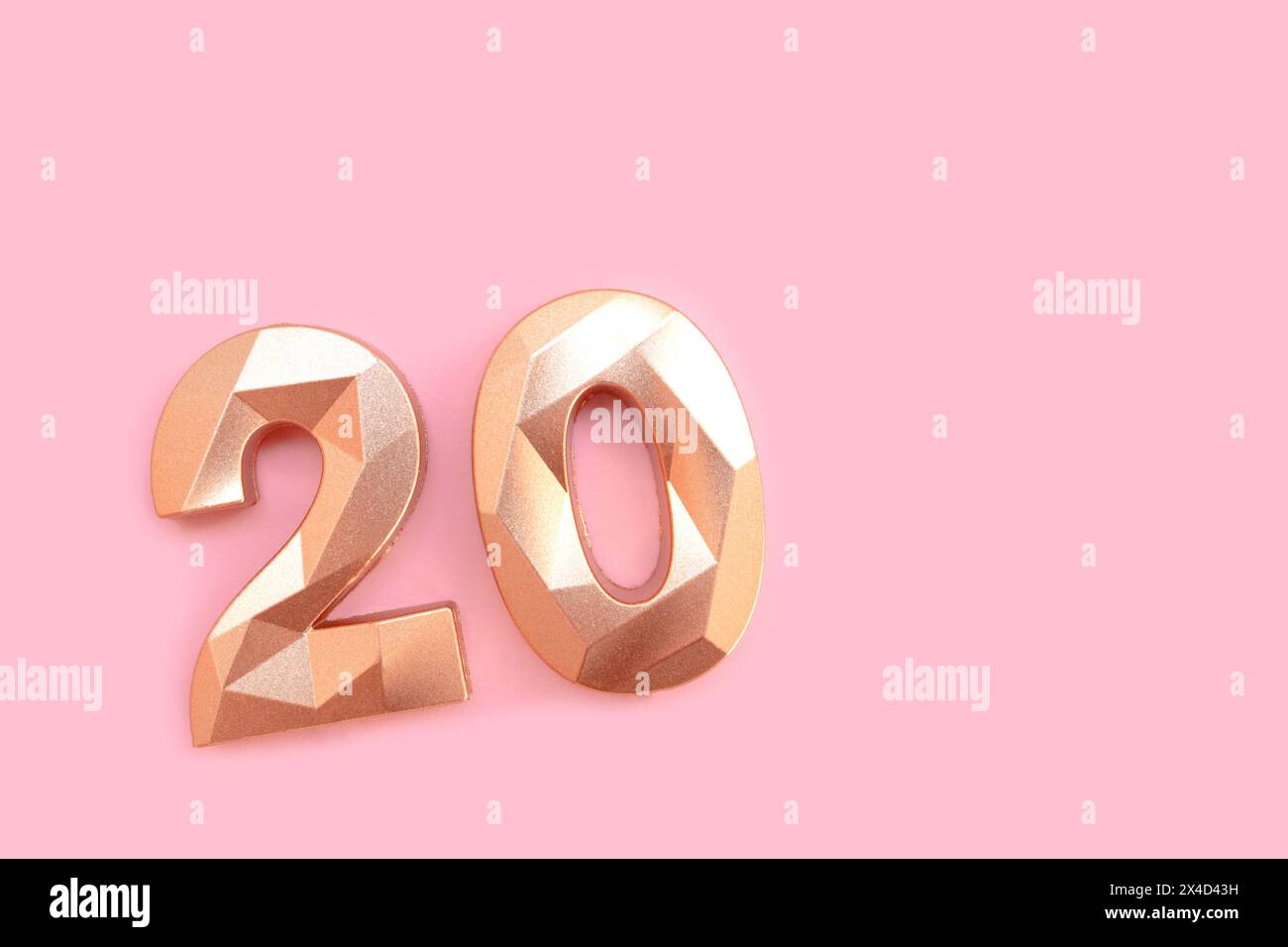 Gold colored number twenty on a pink background with copy space. Stock Photo