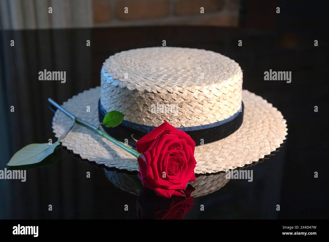 White woven straw hat with a blue ribbon and a red rose on a black background, reflection Stock Photo