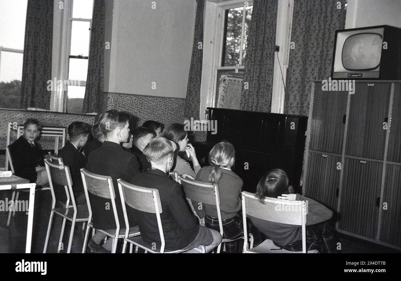 1960s, historical, young children sitting in a school room, watching a programme being broadcast on a television of the era sat high up on some lockers. Stock Photo