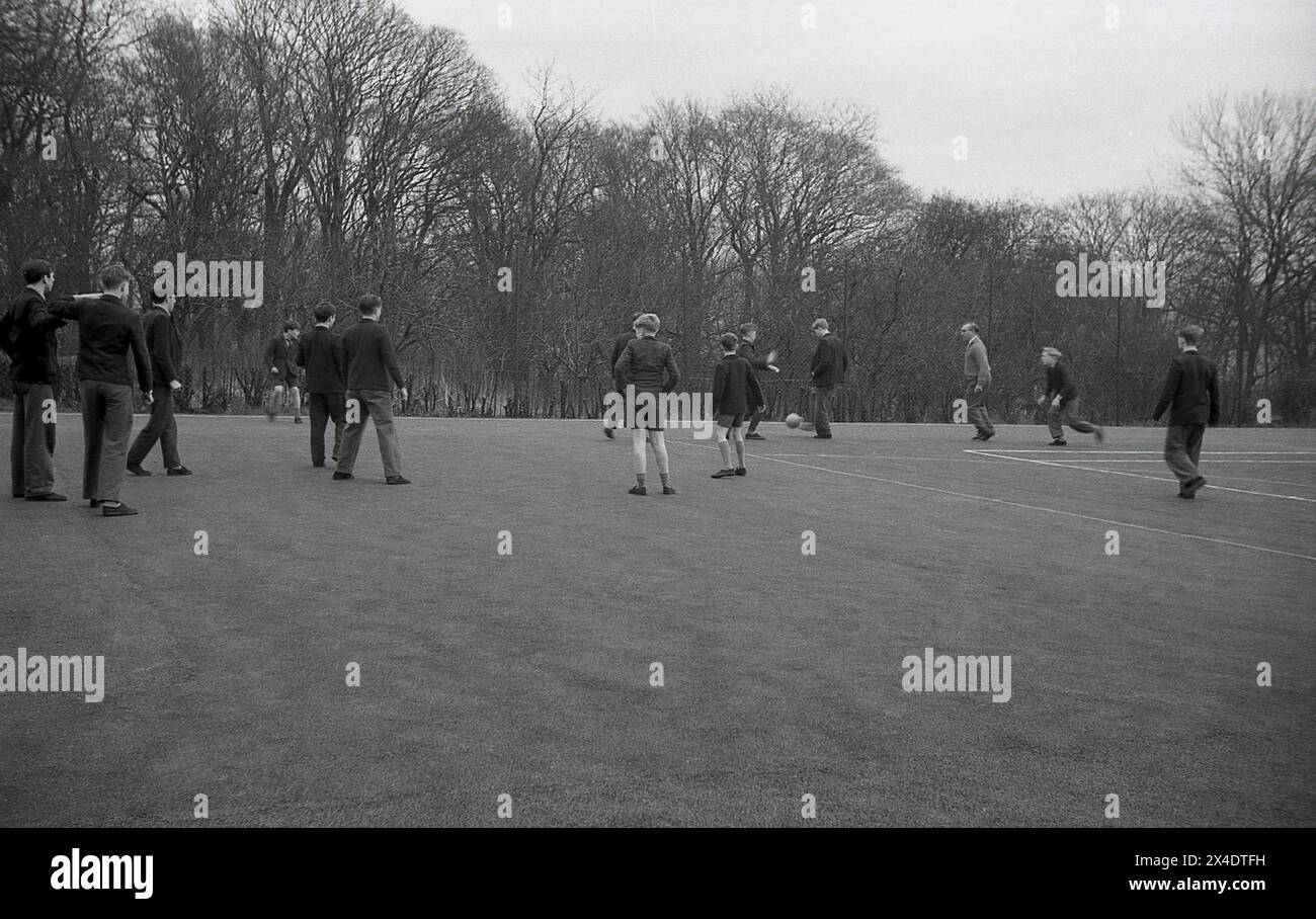 1960s, historical, secondary schoolboys having a kick-about with a football in a concrete playground, a male teacher or master joining in. Stock Photo