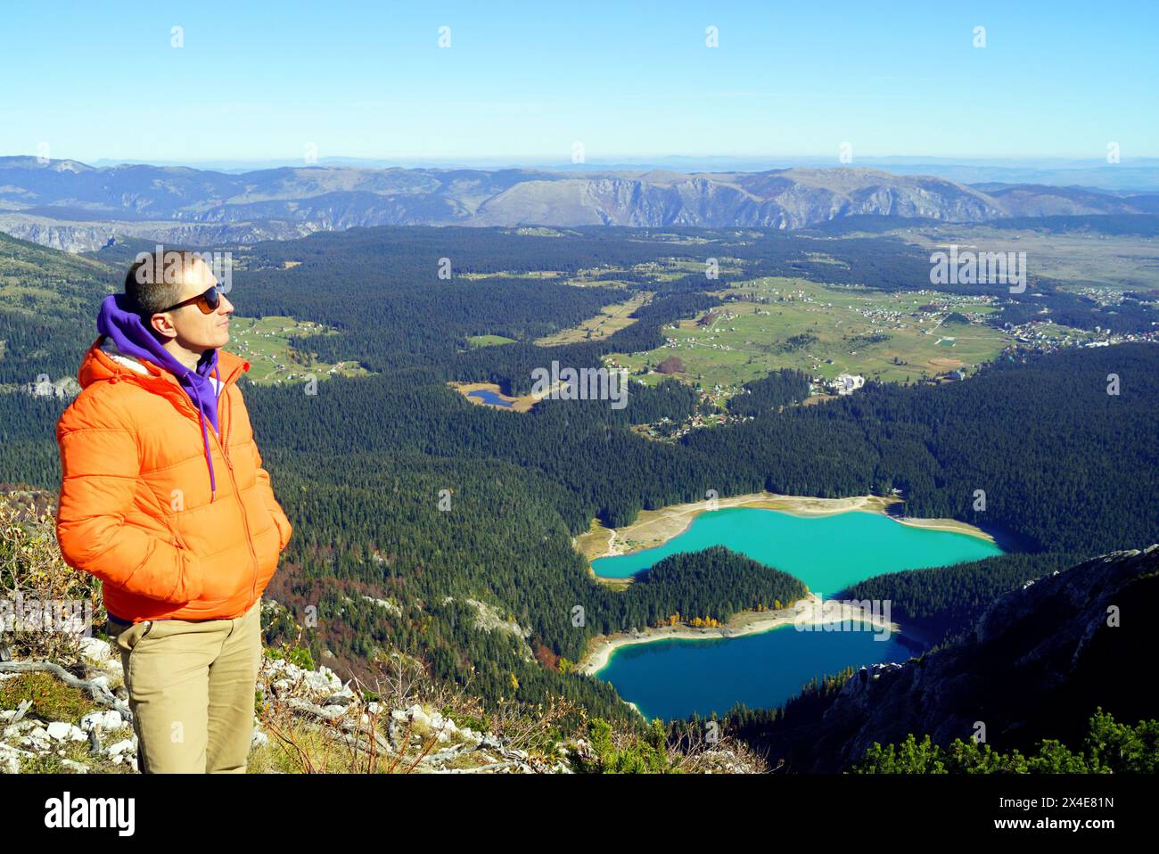 A tourist enjoys the view while standing on top of a mountain with a lake in the background. Portrait of a man in profile during a hike in Durmitor Stock Photo