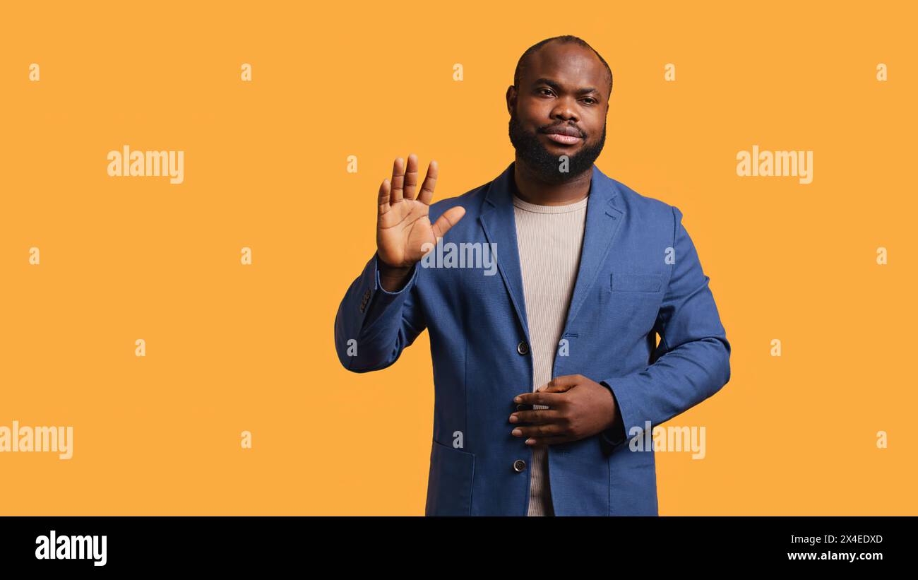 African american man reluctantly doing salutation hand gesture, saying goodbye. Portrait of sad BIPOC person raising arm to greet someone after leaving, isolated over studio background, camera B Stock Photo