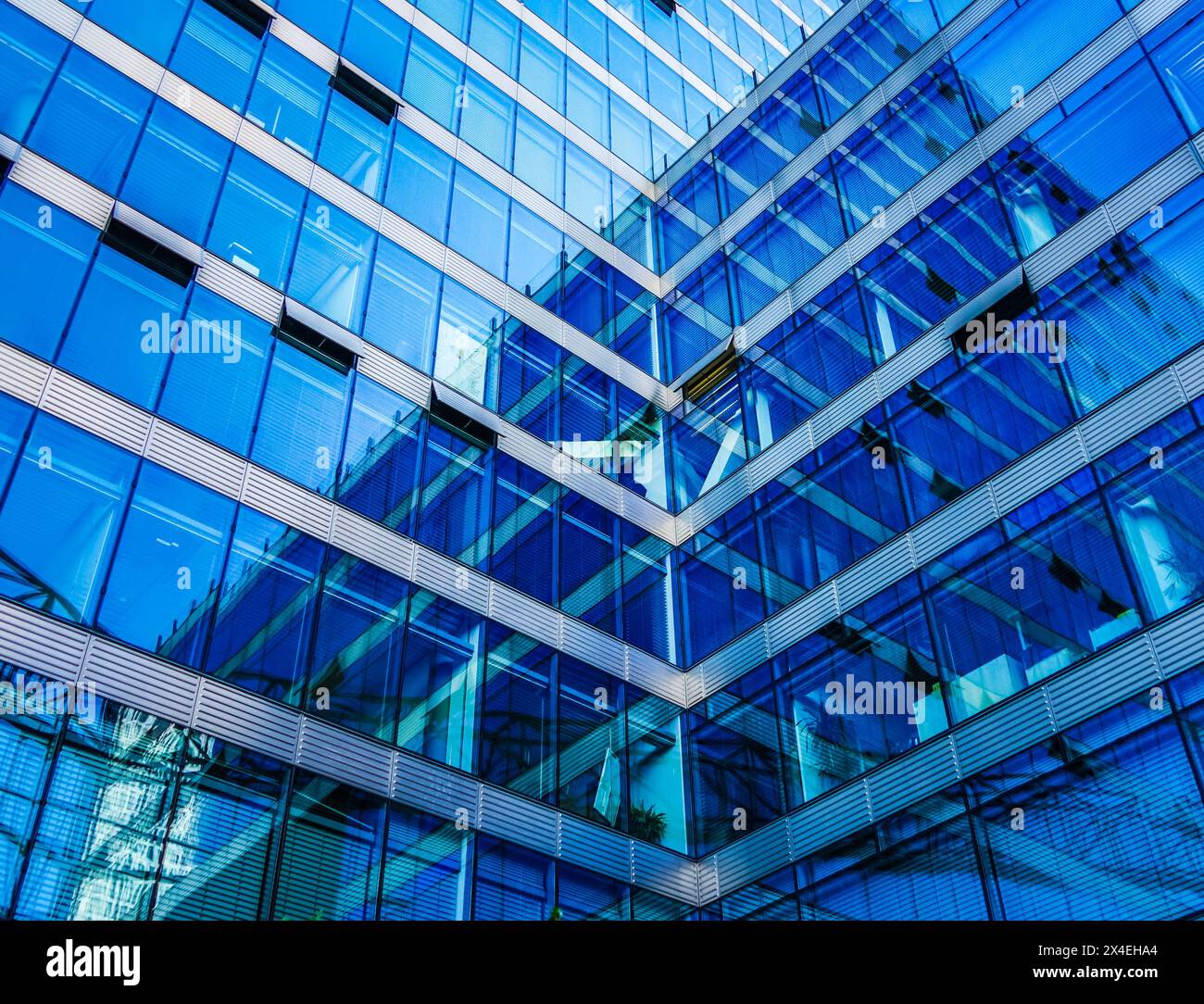 Low angle view of modern glass office building with blue tinted windows and geometric architectural patterns creating abstract reflections. Stock Photo