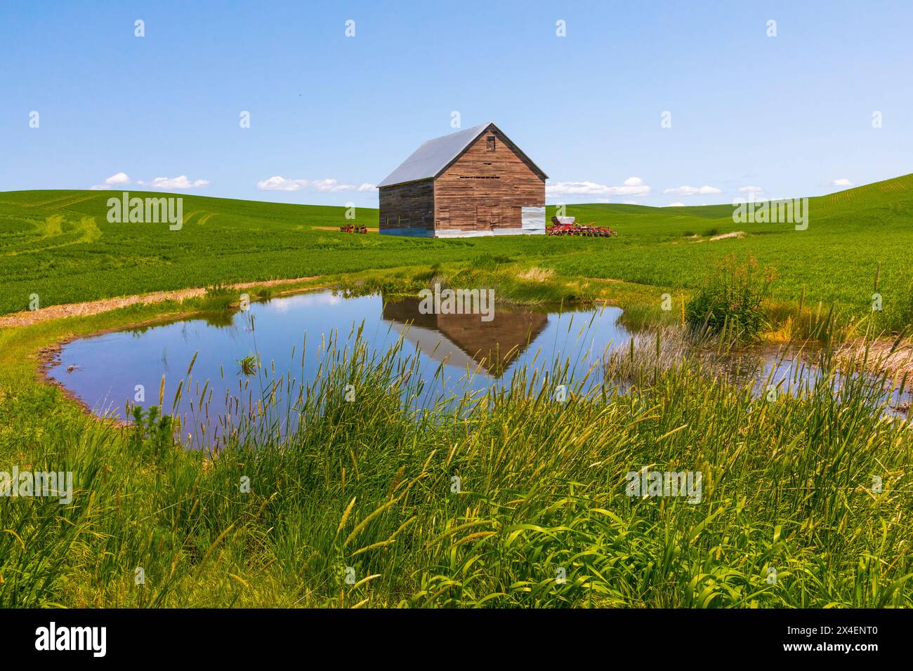 USA, Idaho, Genesee. Brown barn with red farm equipment. Lake Stock Photo