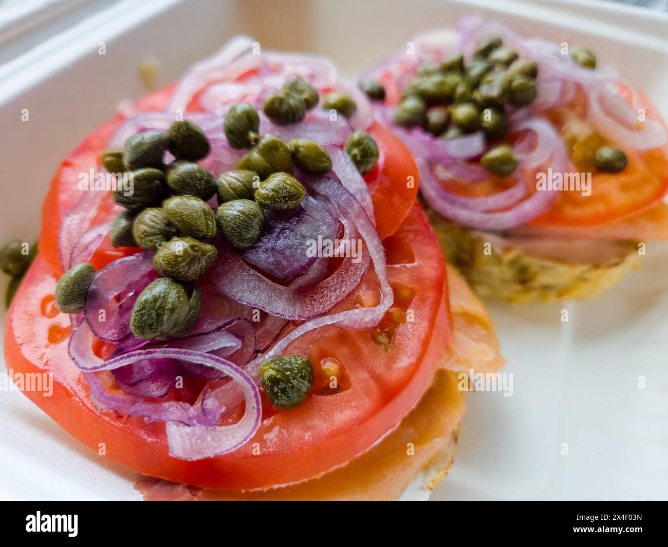 Lox bagel in a to go box with sliced red onions, tomato, and capers
