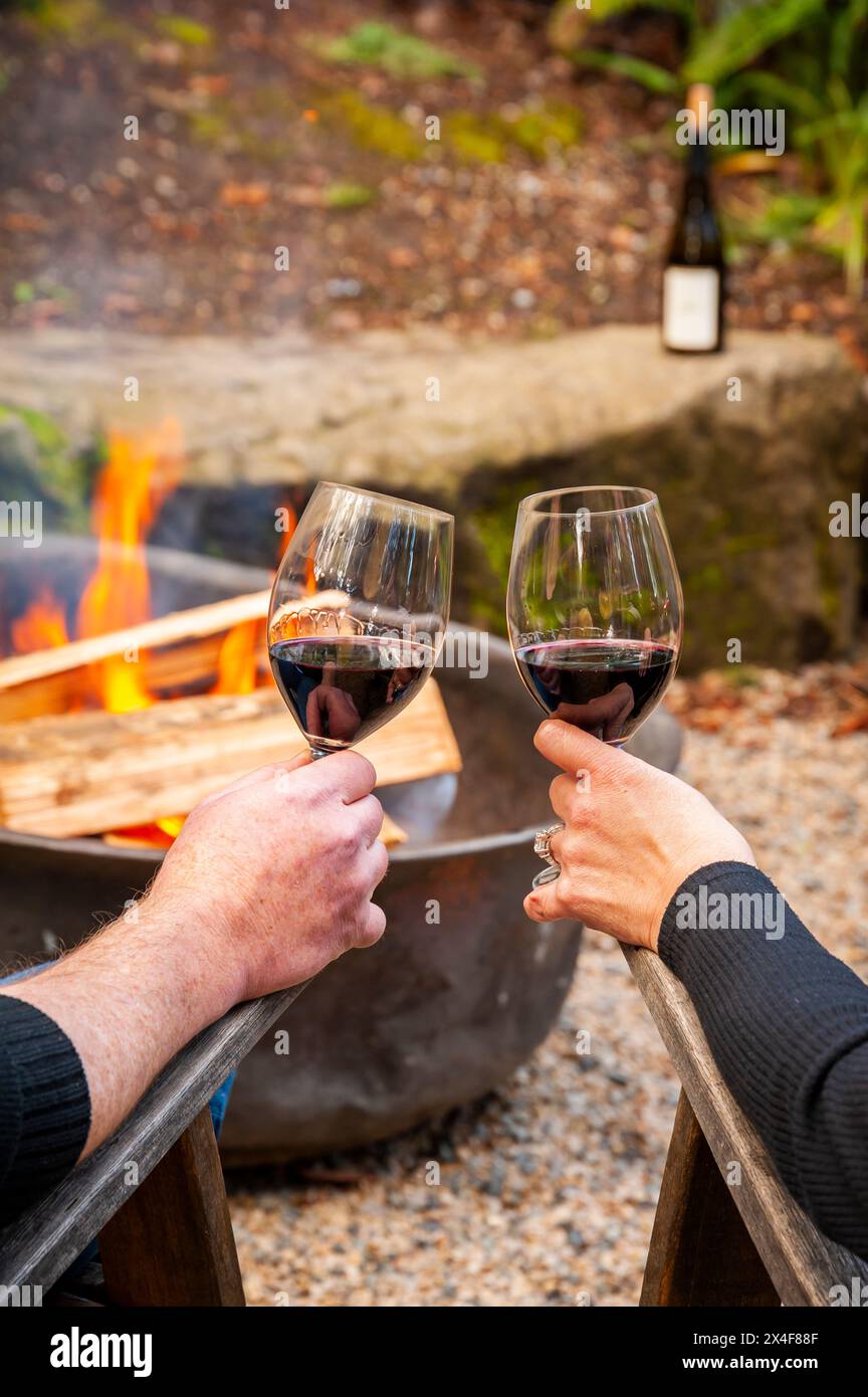 USA, Washington State, Woodinville. A man and a woman enjoy a glass of red wine in front of a campfire. Stock Photo
