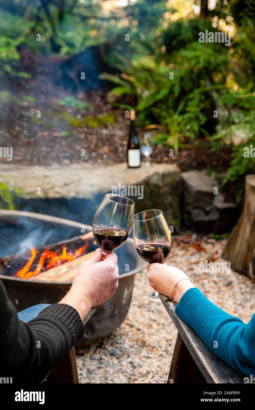 USA, Washington State, Woodinville. A man and a woman enjoy a glass of red wine in front of a campfire. Stock Photo