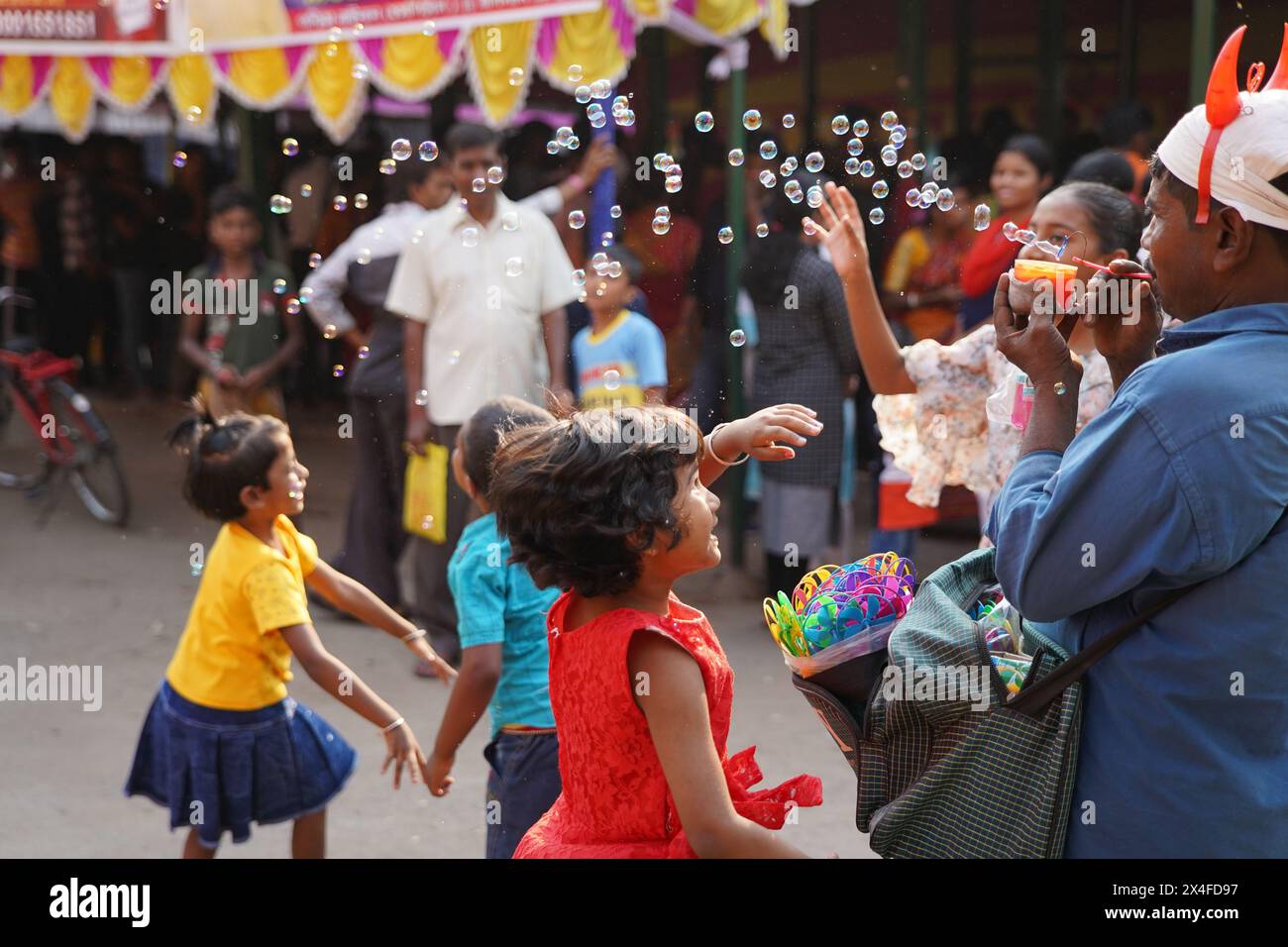 Joyful children dance while a street vendor blows soap bubbles. Bainan Bazaar area, Bagnan, Howrah, West Bengal, India. Stock Photo