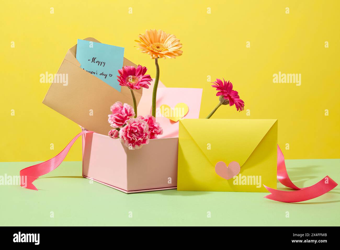 Front view of pink gift box fill with fresh flowers and cute paper cards for women on International Women's Day. Minimalist concept for celebration. B Stock Photo