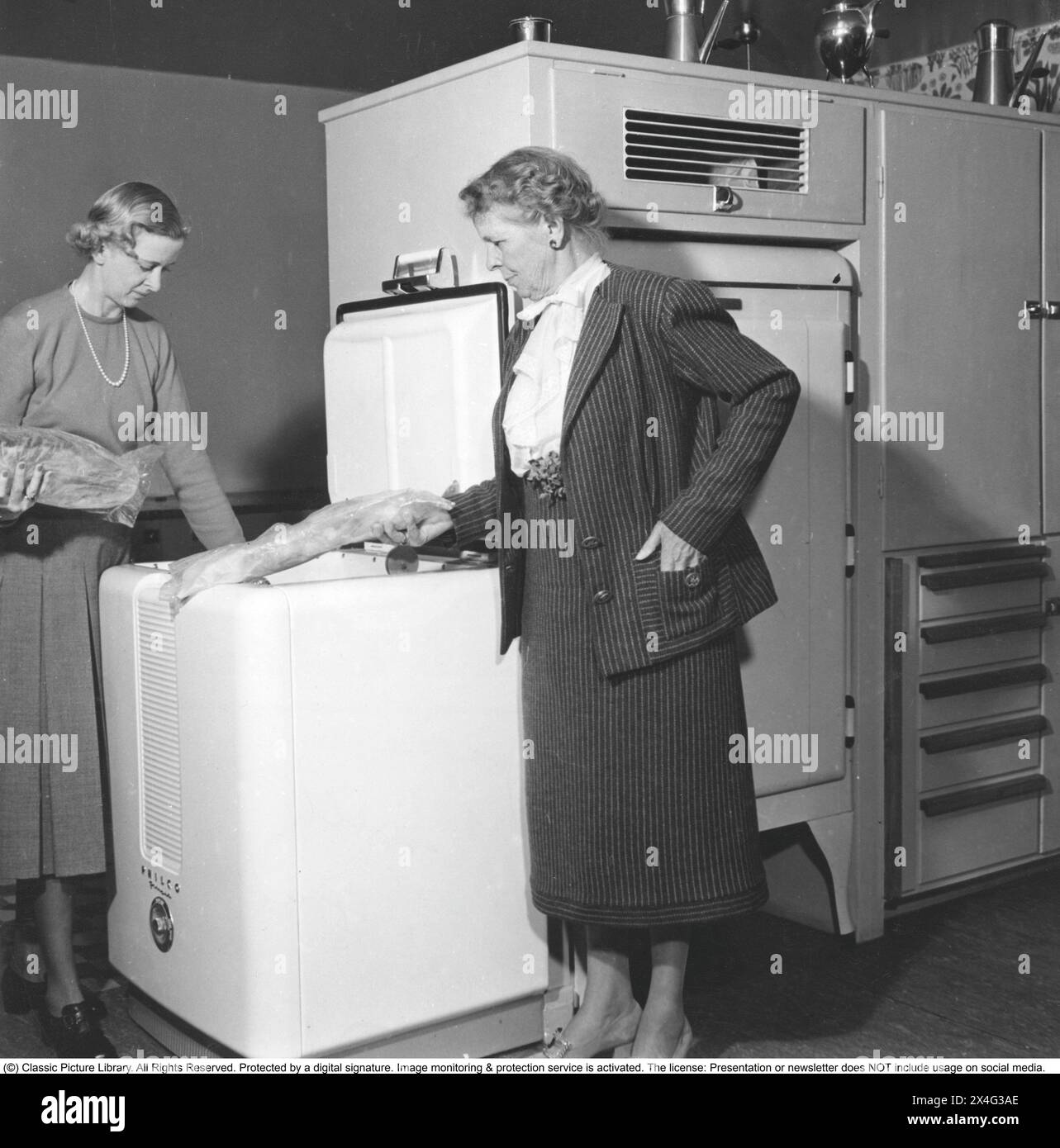 Freezer box in the 1950s. Baroness Märtha Roshall with Baroness Madeleine Leijonhufvud at a freezer from the American manufacturer Philco, where they keep deep-frozen food. Deep-frozen food would be the start of a revolution in household habits and food storage. Many were sceptical, and especially canned food manufacturers considered frozen food to be a passing trend. 1950 Stock Photo