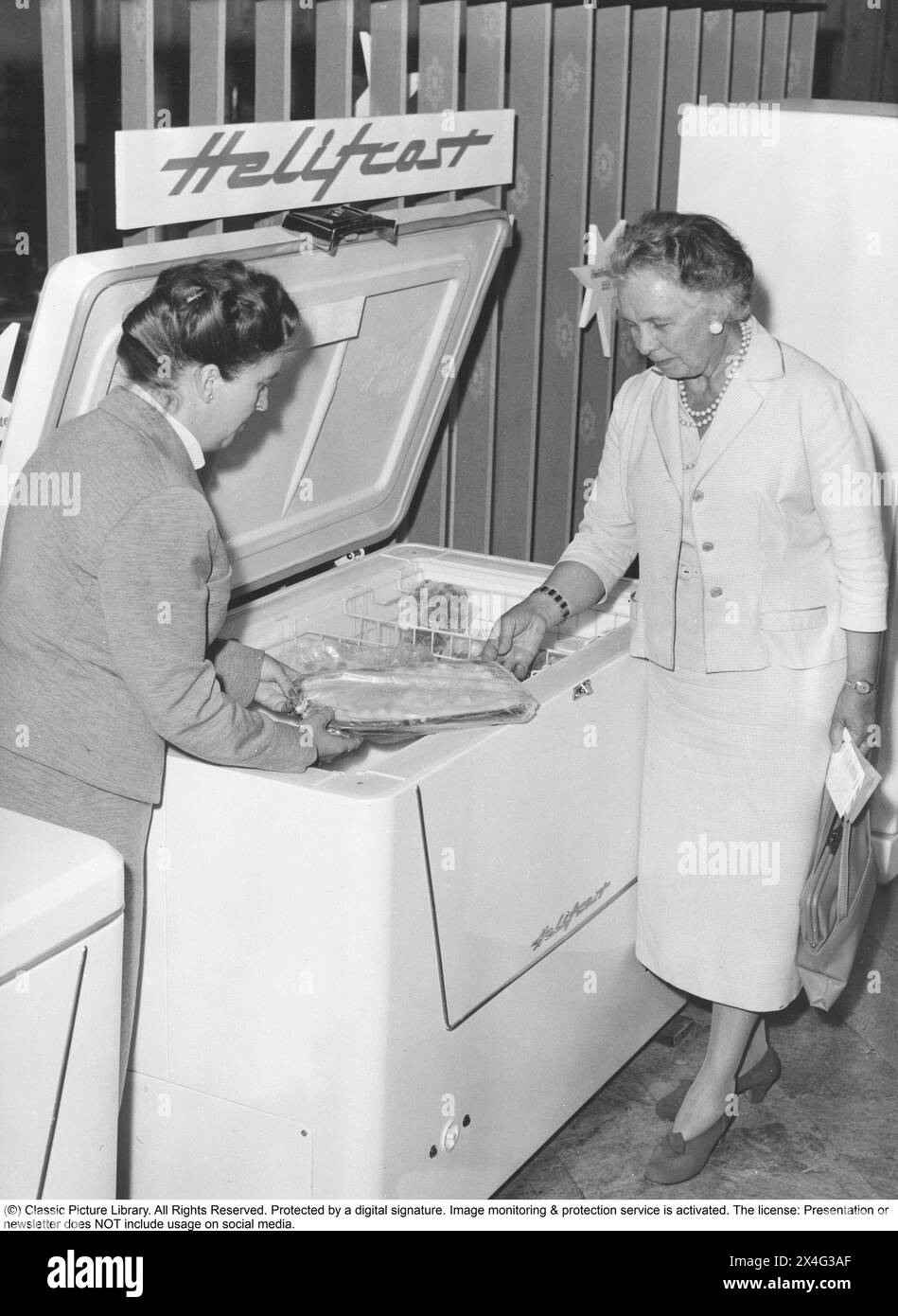 Freezer box in the 1950s. The manager of the appliance manufacturer Elektrohelio's test kitchen Mrs. Eva Göthberg shows a deep-frozen fish gratin to home consultant Ingeborg Lundborg. Deep-frozen food would be the start of a revolution in household habits and food storage. Many were sceptical, and especially canned food manufacturers considered frozen food to be a passing trend. 1955 Stock Photo