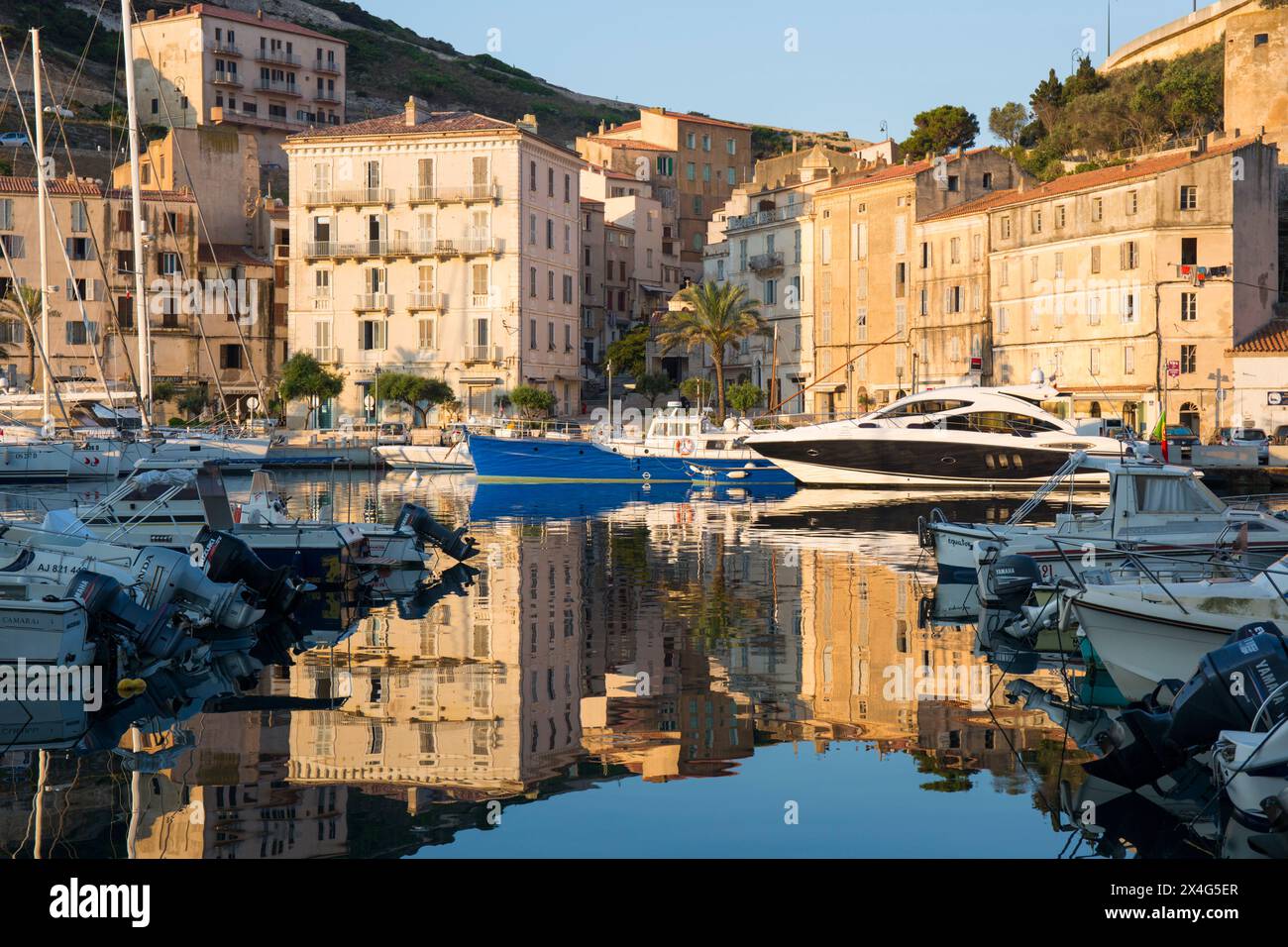 Bonifacio, Corse-du-Sud, Corsica, France. View across the harbour at sunrise, quayside buildings reflected in still water. Stock Photo