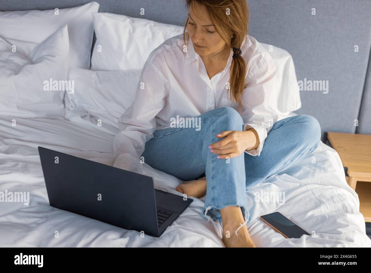 Woman using laptop working on bed at home. Stock Photo