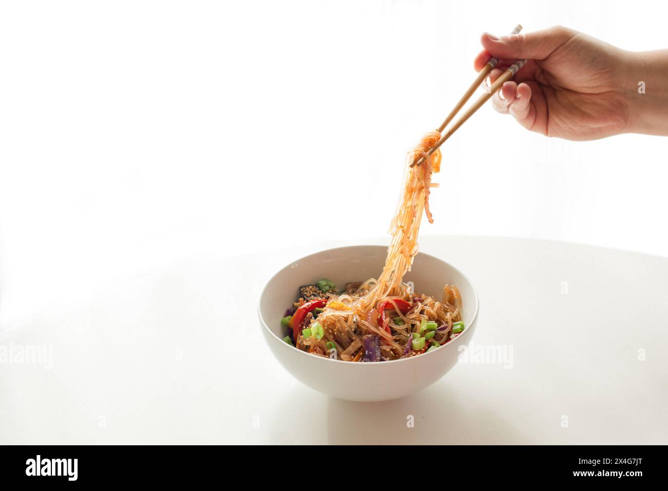 Lifting noodles from bowl with chopsticks Stock Photo