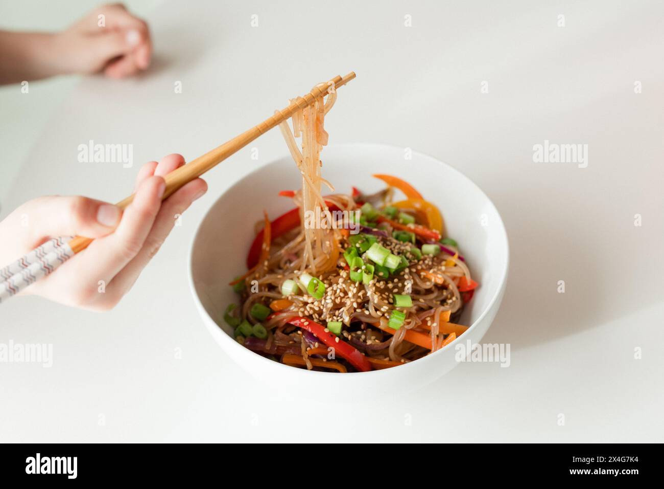 Enjoying a bowl of colorful vegetable noodles with chopsticks Stock Photo