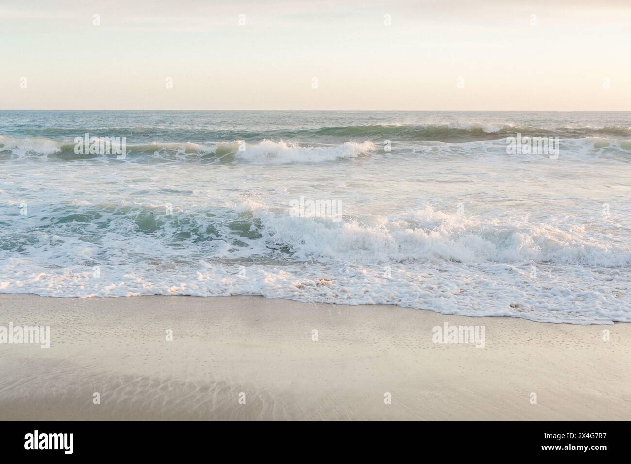 Dynamic waves break on a sunlit, sandy beach Stock Photo