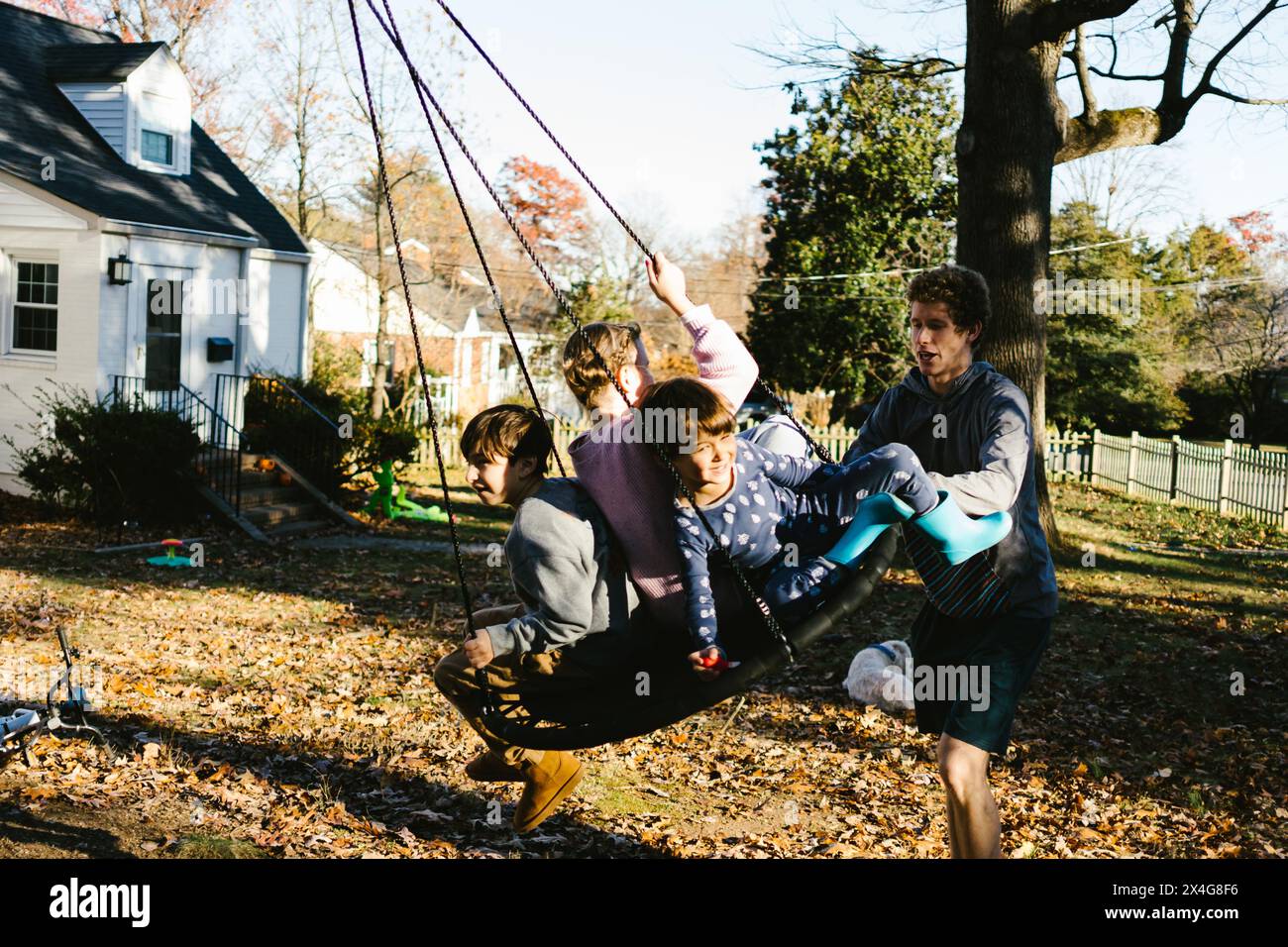 Teenager pushes younger cousins on tree swing in front yard Stock Photo