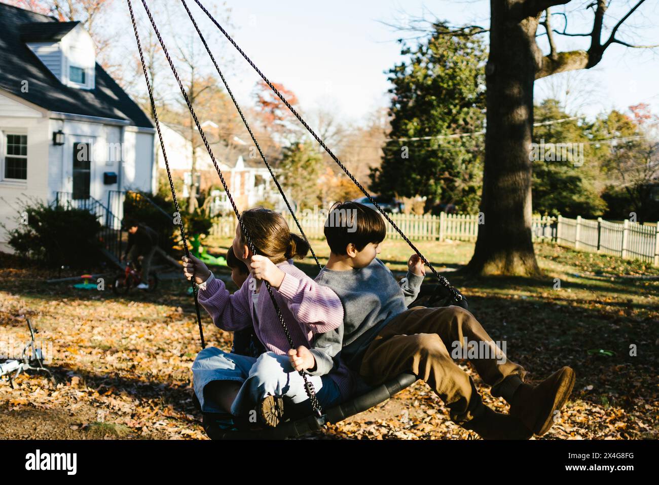 Cousins on tree swing in front yard under trees in autumn Stock Photo