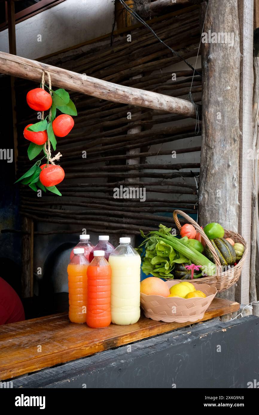 A basket of fresh fruit and vegetables sits next to bottles of j Stock Photo