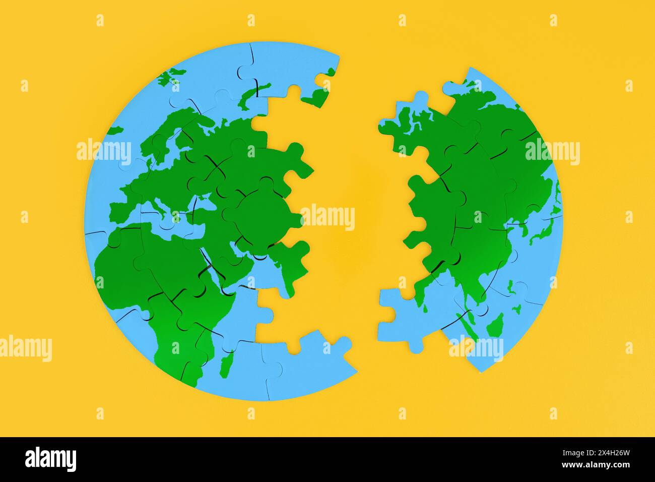 Top view of a globe shaped jigsaw puzzle split into two parts on a vibrant yellow background. Need for unity and the importance of working together. Stock Photo