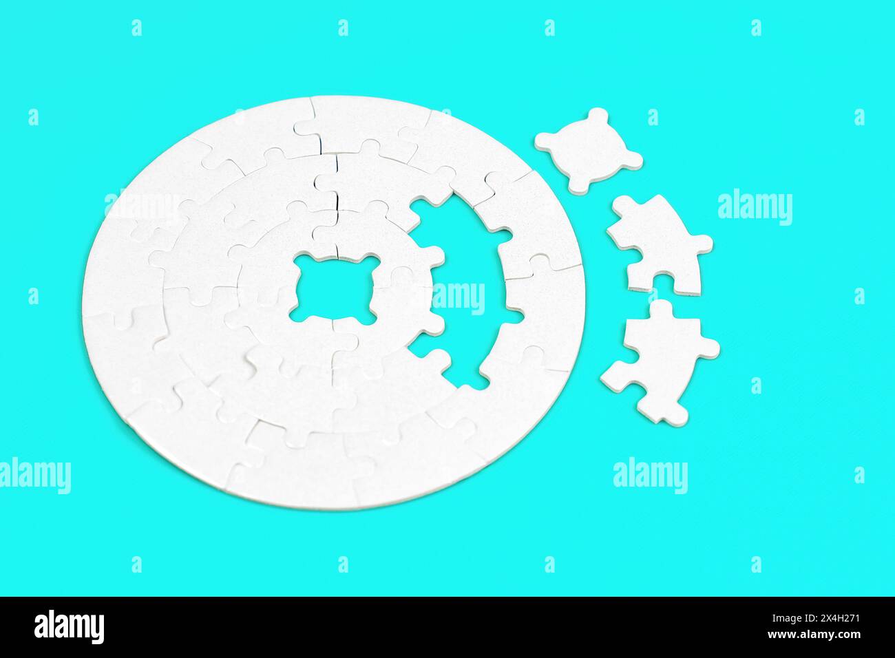 Blank round jigsaw puzzle and three final pieces set aside on a light blue background. Stock Photo
