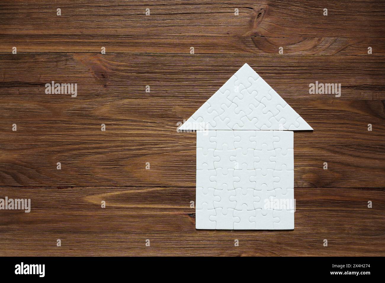 Jigsaw puzzle in the shape of a house with a roof, set against a dark wooden backdrop. Home and family concept. Stock Photo