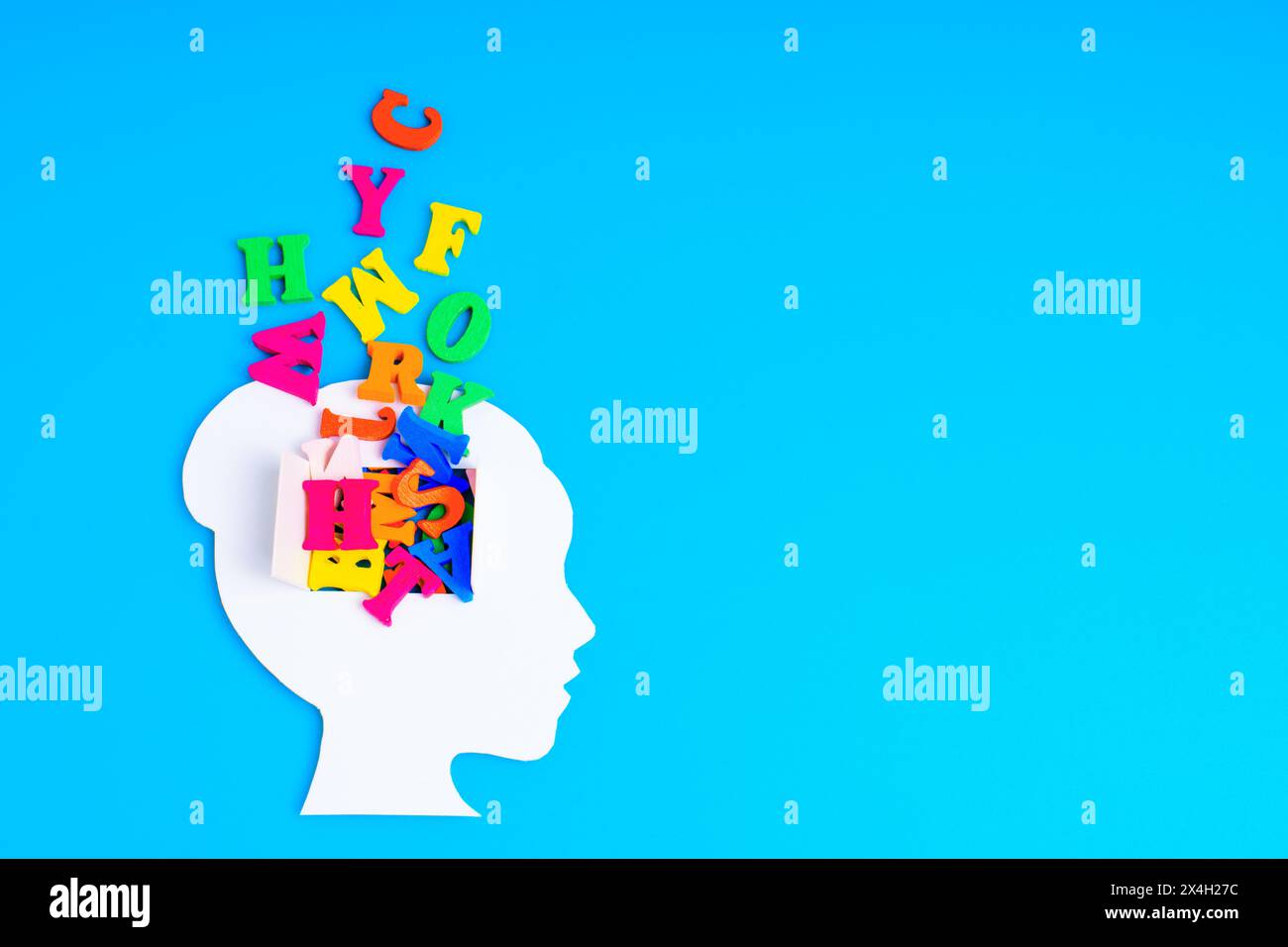 White paper-cut female head, set against a blue backdrop, features a window in the brain area revealing a playful spill of colorful letters. Creativit Stock Photo