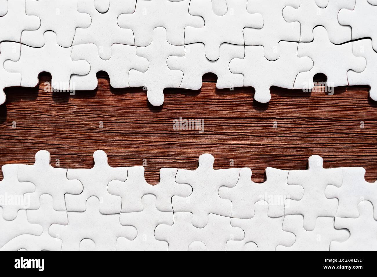 Close-up view of a white blank puzzle with a row of missing pieces, offering a glimpse of a rustic wooden background behind. Stock Photo