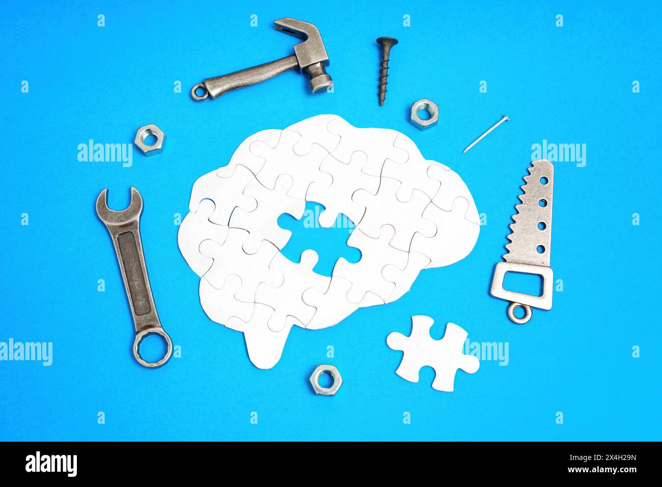 Brain-shaped puzzle with its last missing piece, surrounded by miniature replicas of hand tools including a saw, hammer, wrench, nut, and screw. Probl Stock Photo