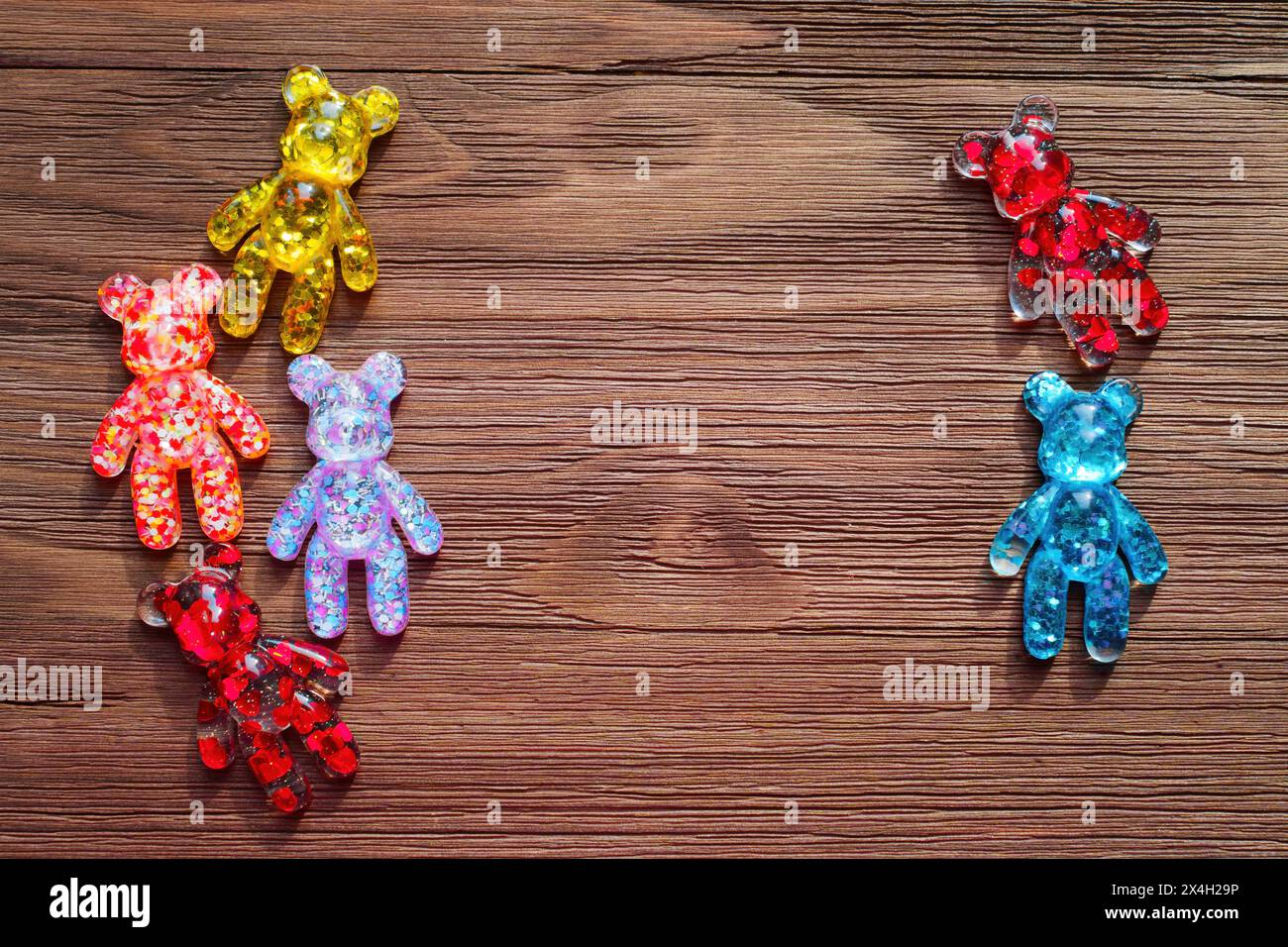 Collection of colorful bear figurines filled with hearts and glitter, arranged on a rustic wooden background, framing some space for text, personalize Stock Photo