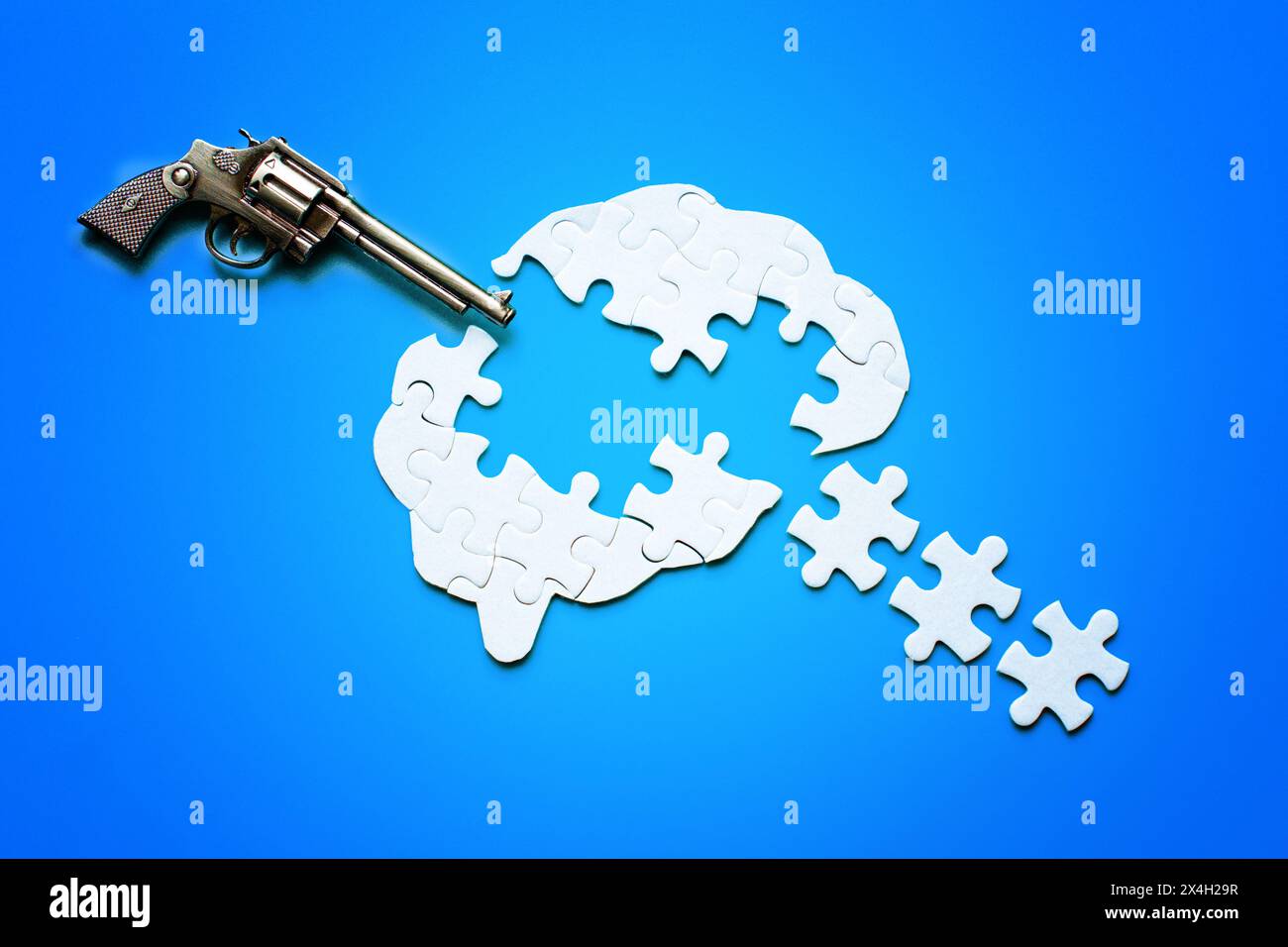 Human brain-shaped puzzle with a gun. Several puzzle pieces are displaced from the puzzle, simulating the effect of a gunshot. Violence and psychologi Stock Photo