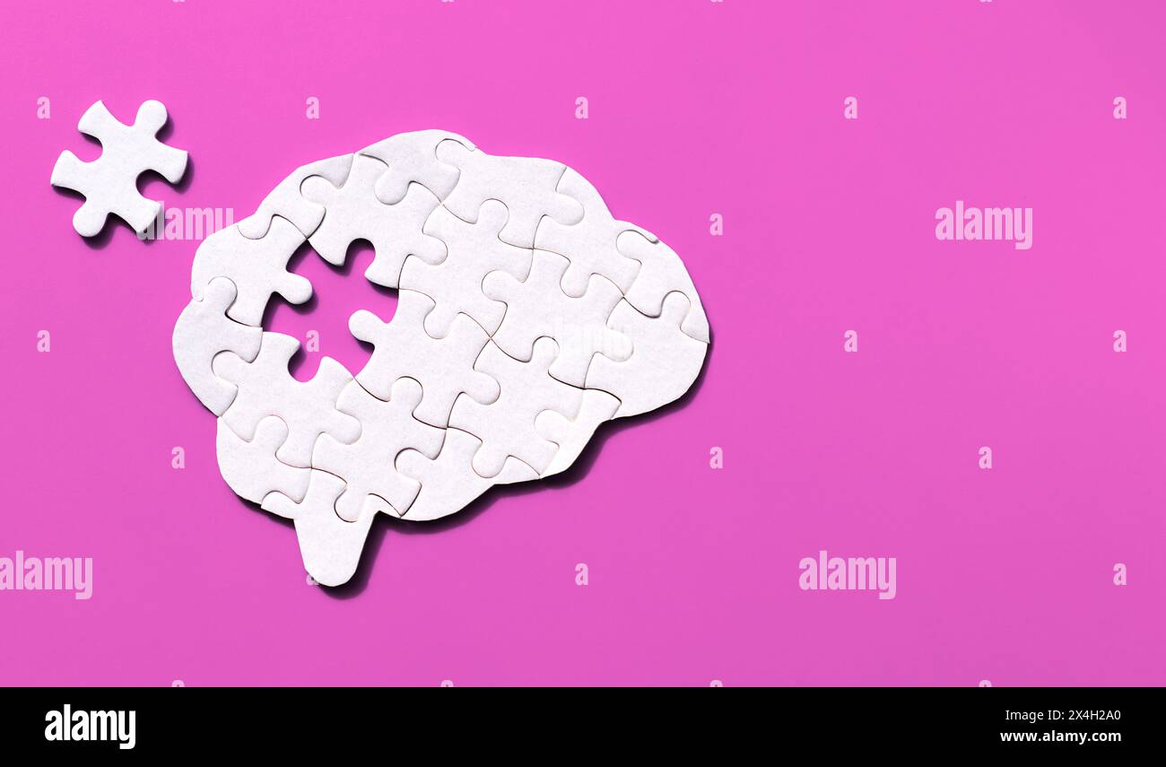 Brain-shaped puzzle with a missing element arranged on a soft pink background with copy space. Human mind complexity concept. Stock Photo