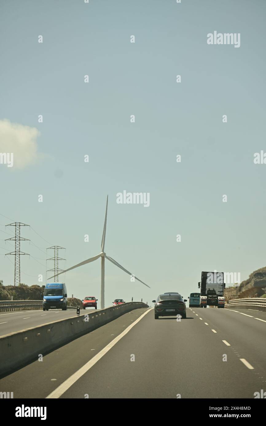 busy highway with cars, a wind turbine, and power lines, capturing the contrast between modern technology and traditional infrastructure Stock Photo
