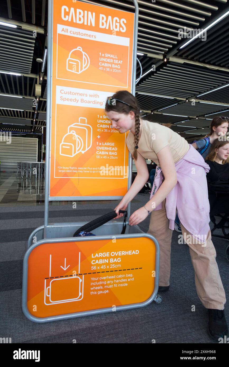12 Year old girl / child / kid & Easyjet bag size frame cage tester to measure dimensions of passenger hand held carry on flight luggage checking in for an Easy Jet flight. (138) Stock Photo