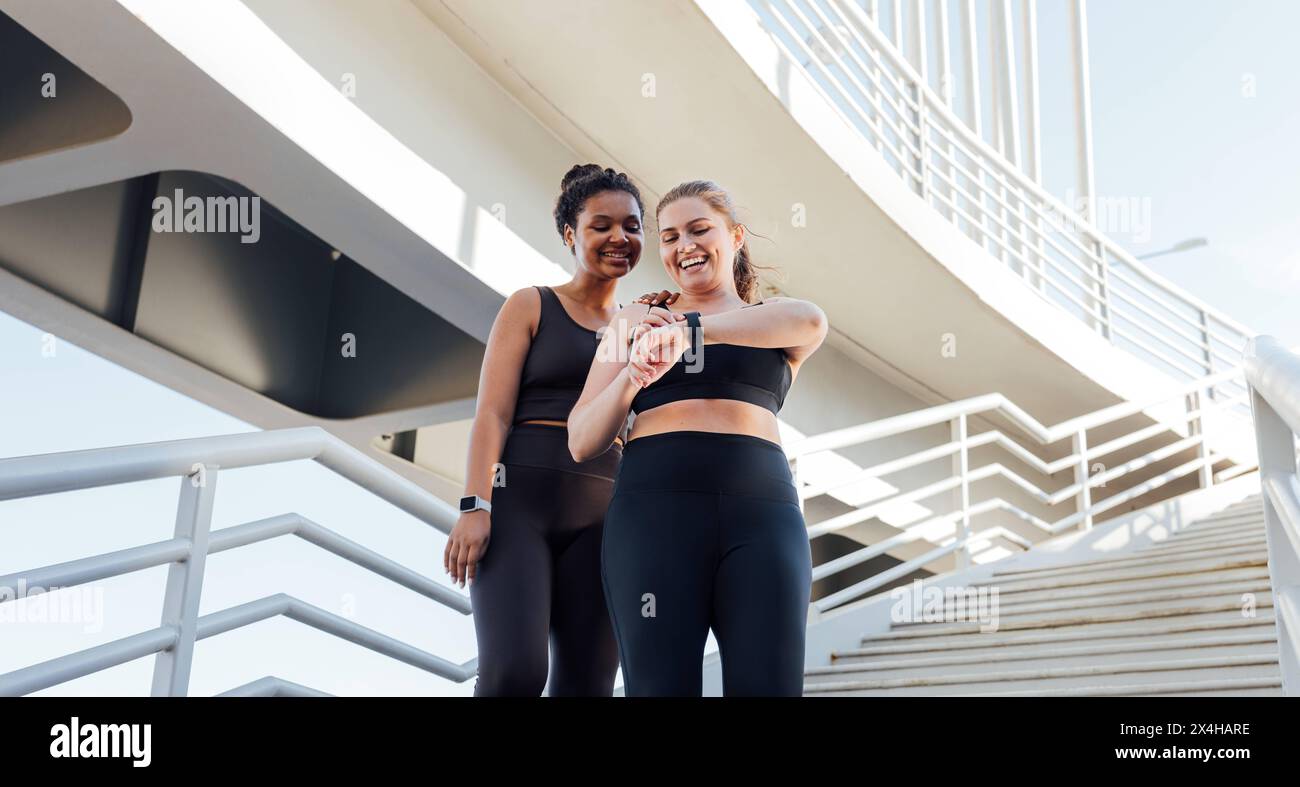 Happy plus-size woman showing her friend workout results on smartwatches. Two friends in sportswear looking at smartwatches. Happy plus-size woman sho Stock Photo