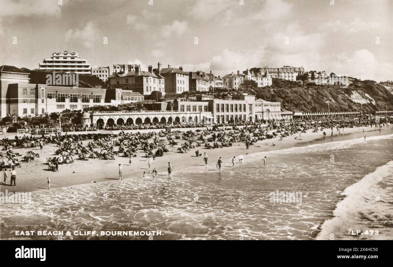 Dorset, England. Circa. 1952. An antique postcard entitled “The East Beach & Cliff, Bournemouth” depicting the East Beach, very busy with holidaymakers and tourists. Stock Photo