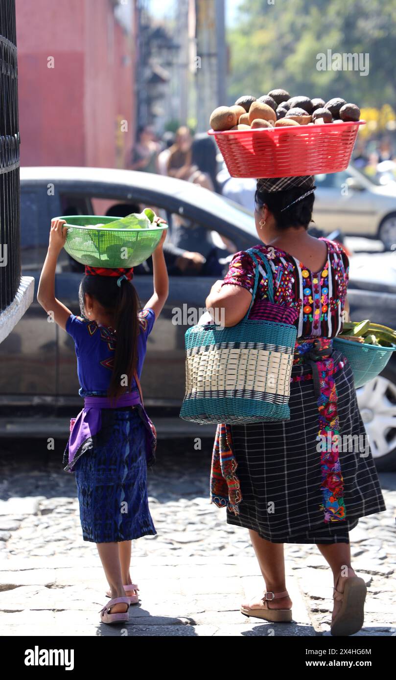 Indigenous Mayan mother and child-off to market. Both in native costume, carrying produce in bowls on their heads, Antigua, Guatemala, Central America Stock Photo