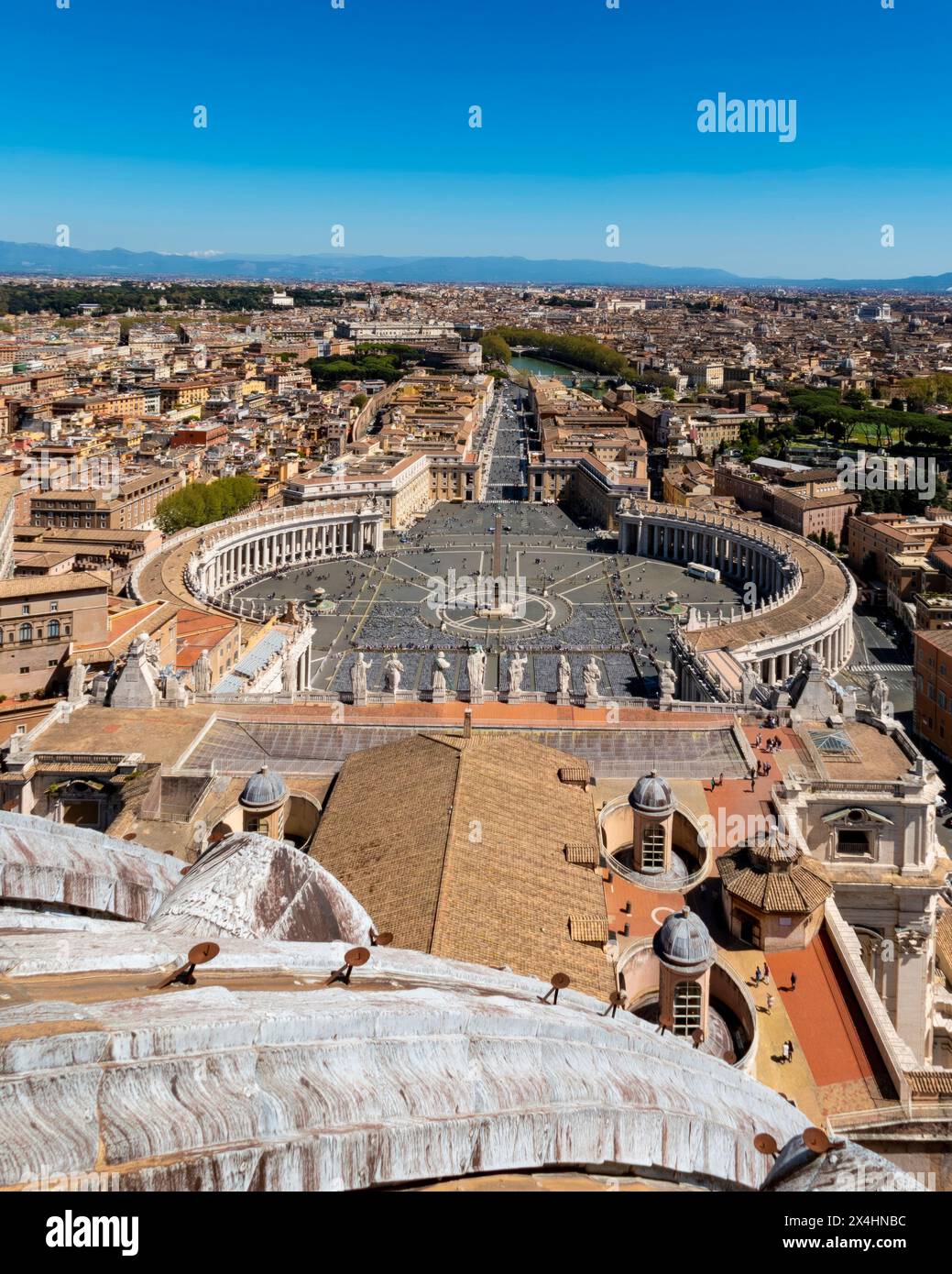 Aerial view of St. Peter's Square in Vatican City, showcasing the iconic oval colonnades and central obelisk, with Rome's cityscape in the background. Stock Photo