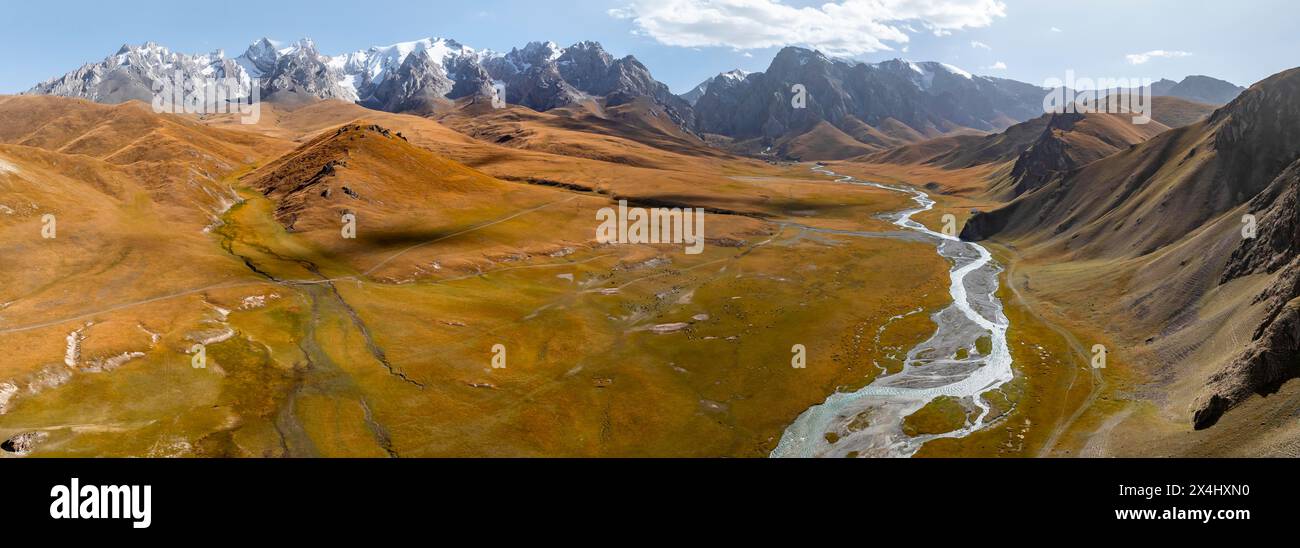 Aerial view, River Kol Suu winds through a mountain valley with hills covered with yellow grass, Pointed high mountain peaks with glaciers, Keltan Stock Photo