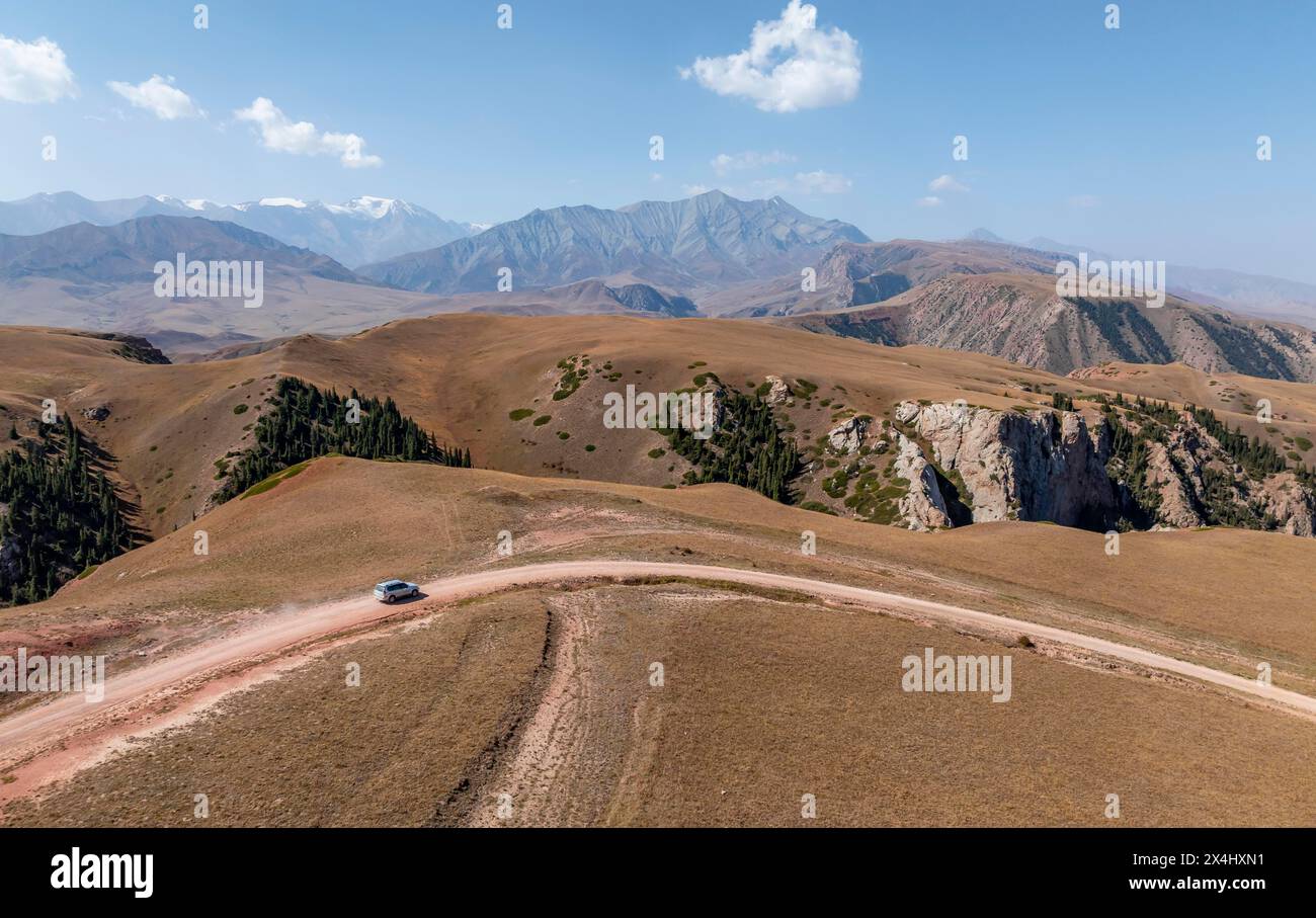 Moldo-Ashuu Pass, car on road between yellow hills, near Baetov, Naryn region, Kyrgyzstan Stock Photo